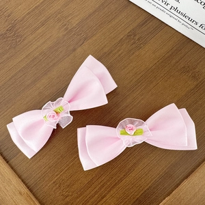 Détails de barrettes à nœud en satin rose avec petites roses sur fond bois sombre