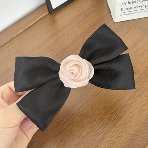 Dettaglio di un fermaglio per capelli in raso nero con rosa di stoffa su sfondo legno