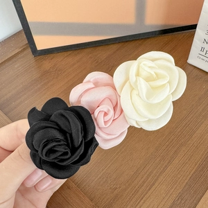 Gros plan sur trois pinces à cheveux camélia en soie faites main en noir, rose et crème