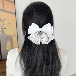 Close-up of white satin bow hair clip with embroidered lace detail on dark hair