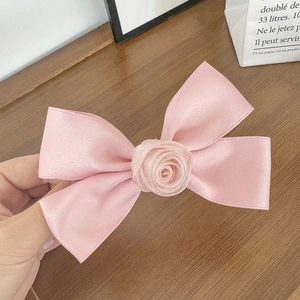 Dettaglio del fermaglio per capelli con fiocco di raso rosa e fiore di rosa strutturato