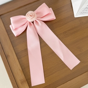 Détail d'un nœud de cheveux en satin rose avec rose en tissu sur fond en bois clair