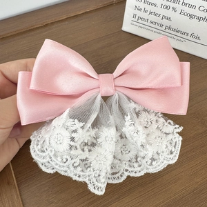 Close-up of pink satin ribbon bow with white floral lace embroidery detail on wood