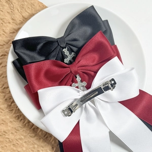 Three satin bow hair clips in black, red, and white with vintage metal cross pendants