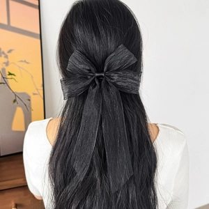 Detail of elegant black oversized mesh bow hair clip with long ribbons on wavy hair