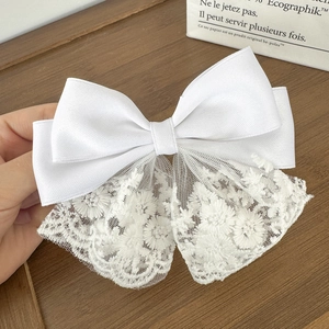 Detail view of a white lace bow hair clip featuring fine floral embroidery and silk satin