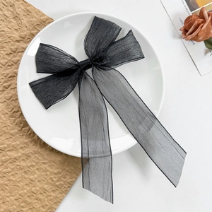 Detail of elegant black mesh bow hair clip with long ribbons on a white porcelain plate