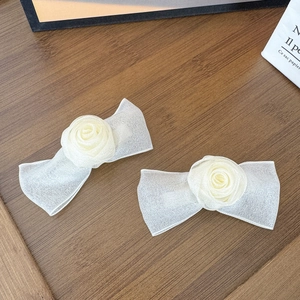 Detail von cremeweißen Organza-Rosen-Haarspangen auf einem strukturierten Holzboden