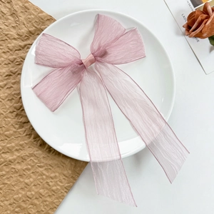 Macro view of light pink organza bow hair clip with long ribbons on white plate