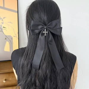 Detail of a black satin bow hair clip with a silver cross pendant on wavy dark hair