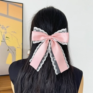 Elegant pink satin bow hair clip with white lace trim worn on long dark hair