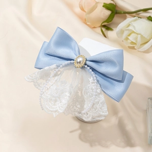 Close-up of blue satin bow hair clip with white lace trim and oval faux pearl detail