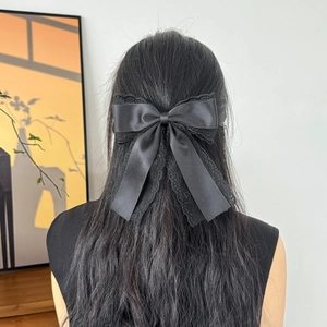 Detail view of a black lace bow hair clip worn as a stylish half-up ponytail accessory