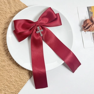 Detailed macro view of burgundy satin bow hair clip featuring a silver gothic cross pendant