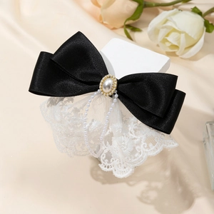 Close-up of a black satin bow hairclip with floral lace, pearl center, and tassels