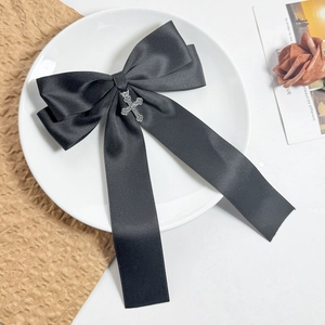 Detailed macro view of black satin bow hair clip with vintage silver cross charm