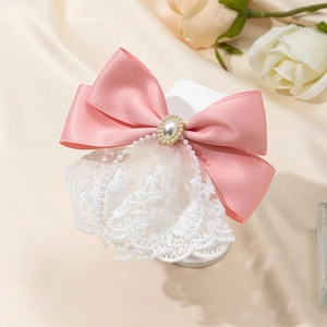 Detailed view of pink satin bow hairpin with white lace, pearls, and bead chains