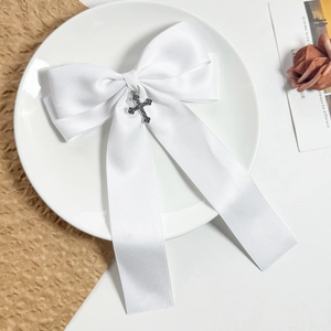 Detail of a large white satin bow hair clip with a vintage silver cross pendant detail