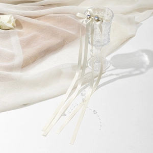 Sweet cream ribbon hair clip with bow, heart gems and pearls hanging on a crystal glass