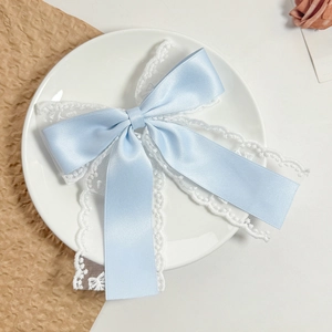 Close-up of light blue satin and white lace bow hair clip on a white ceramic plate