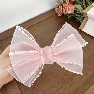 Pince à cheveux nœud en organza rose avec bordures perlées blanches sur fond bois