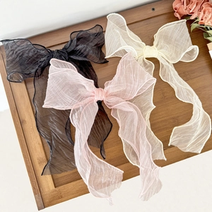 Three elegant oversized organza bow hair clips in black, pink, and beige on wooden stand