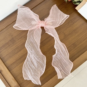 Close-up of pink tulle bow hair clip with long ribbons on a rustic wooden tray