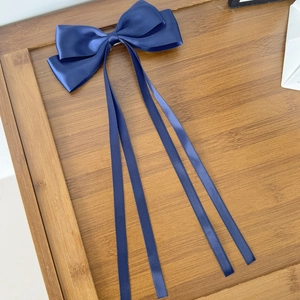 Détail d'une pince à cheveux à nœud en satin bleu foncé avec quatre rubans sur du bois