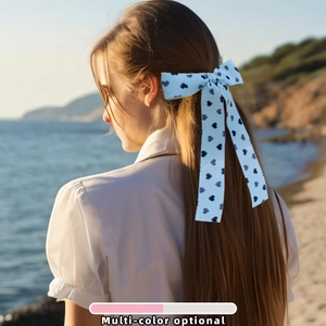 Pince à cheveux noeud bleu clair avec motifs coeurs noirs portée sur la plage au coucher du soleil