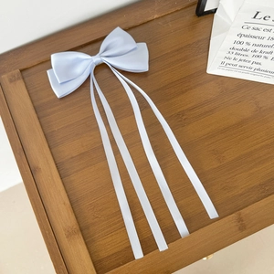 Détail de barrette à nœud bleu clair avec longs rubans soyeux sur plateau bois