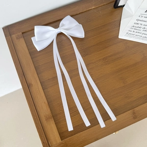 Détail d'une pince à cheveux avec nœud en satin blanc et longs rubans sur bois