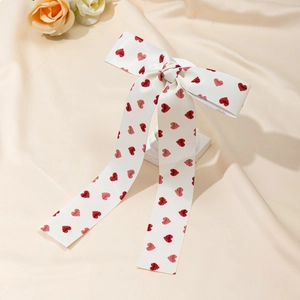 Détail d'une pince à cheveux avec nœud en satin blanc à motifs cœurs rouges et rubans