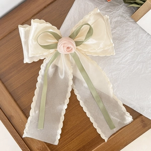Elegant cream mesh bow hair clip with a pink rose centerpiece on a dark wood tray
