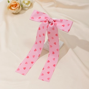 Détail d'une pince à cheveux nœud en satin rose avec motifs cœurs sur fond beige