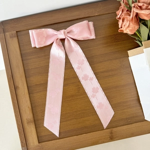 Rosa Satin-Haarspange mit floralem Muster und langen Bändern auf dunklem Holzgrund