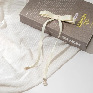 Détail d'un nœud à cheveux crème avec longs rubans et pendentifs perles élégants au bout