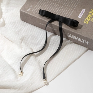 Gros plan d'une barrette à ruban en soie noire avec pendentifs perles sur un livre