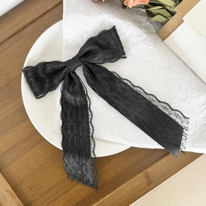 Close-up of elegant black lace bow hair clip with long ribbons on artistic background