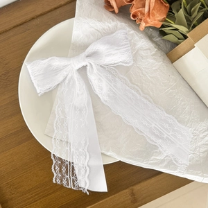 Elegant white lace bow hair clip with long ribbons on a decorative ceramic plate