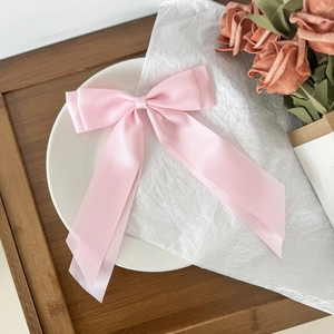 Detail of pink satin bow hair clip with long ribbons on a minimalist white ceramic plate