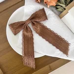 Detail of coffee lace bow hairpin with elegant long ribbons and wavy lace edges