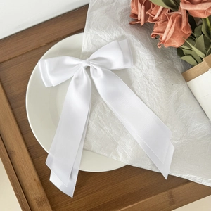 Elegant white satin bow hair clip with long ribbons on decorative tray with pink flowers