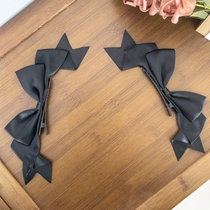 Pair of black satin ribbon bow hair clips with double layers on a wooden tray