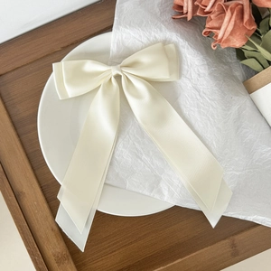 Detailed close-up of a cream satin bow hair clip with elegant long ribbon streamers