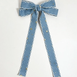 Detailed view of denim bow hair clip with golden stars and white scalloped edge