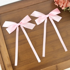 Barrettes à nœuds en satin rose avec longs rubans sur un plateau en bois et une rose