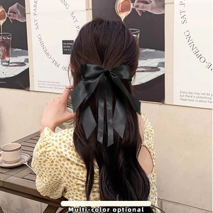 Elegant black satin bow hair clip with long ribbons shown on wavy hair from back