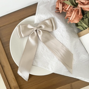 Detail of elegant champagne satin bow hair clip with long ribbons on a textured backdrop