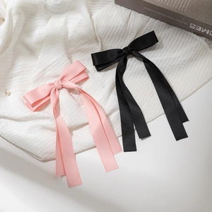 Pink and black ribbon bow hair clips with long streamers on white textured cloth