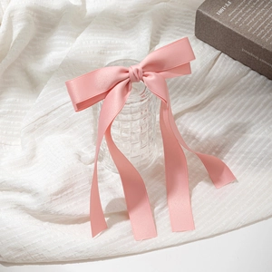 Pink satin ribbon bow hair clip on a white fabric background with elegant props